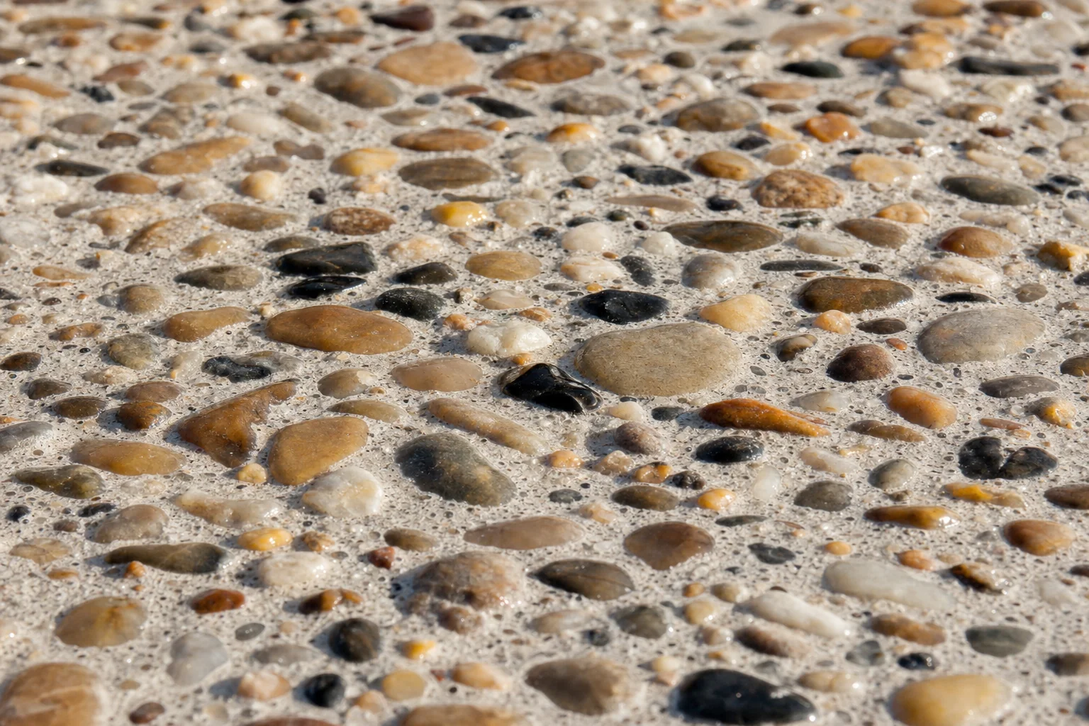Close-up of exposed aggregate concrete texture with river stone and quartz, sealed
